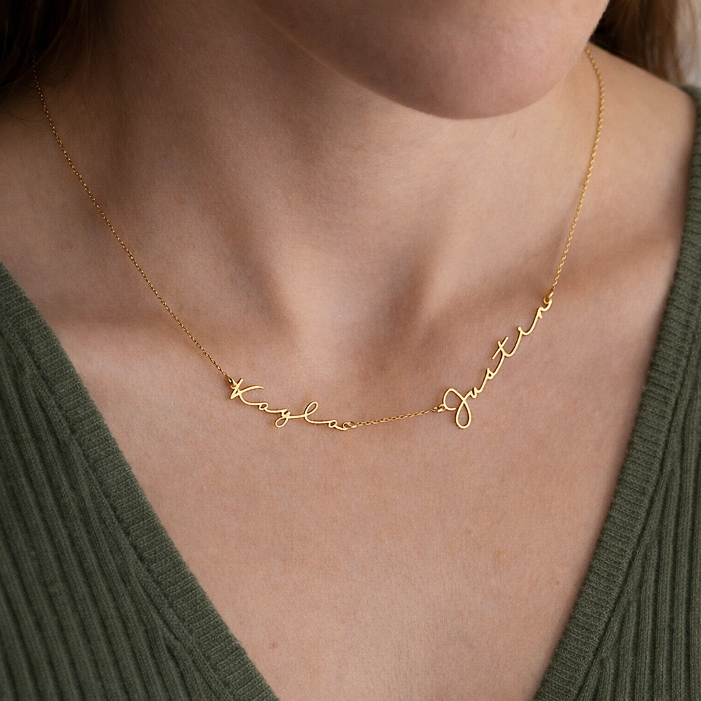 Gold necklace with engraved names on a person wearing a green top